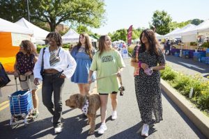 Five market shoppers stroll through Easton Farmers' Market with a pup on a leash.
