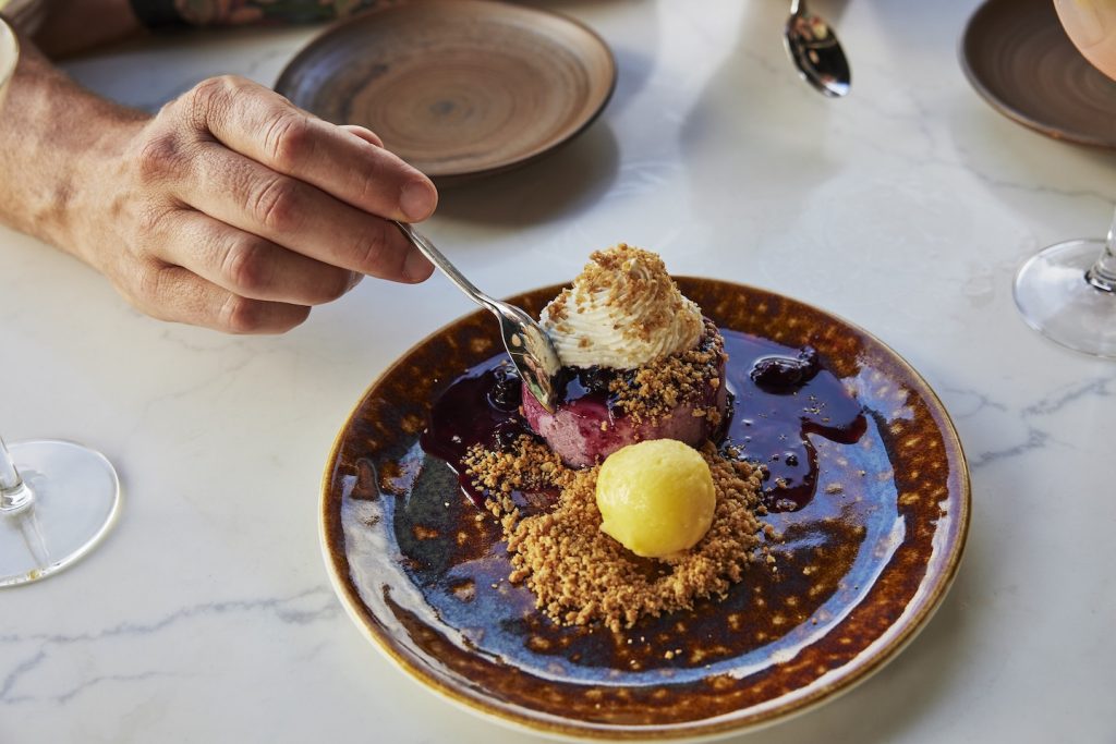 A diner uses a spoon to dig into a berry cheesecake.